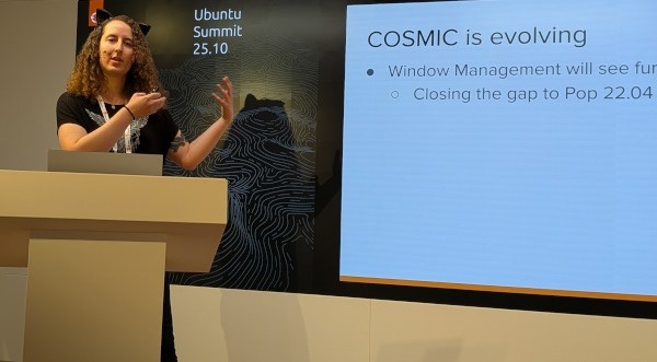 Victoria steht am Pult und gestikuliert mit den Händen. Auf einer Leinwand hinter ist die Präsentation, wo steht "COSMIC is evolving"