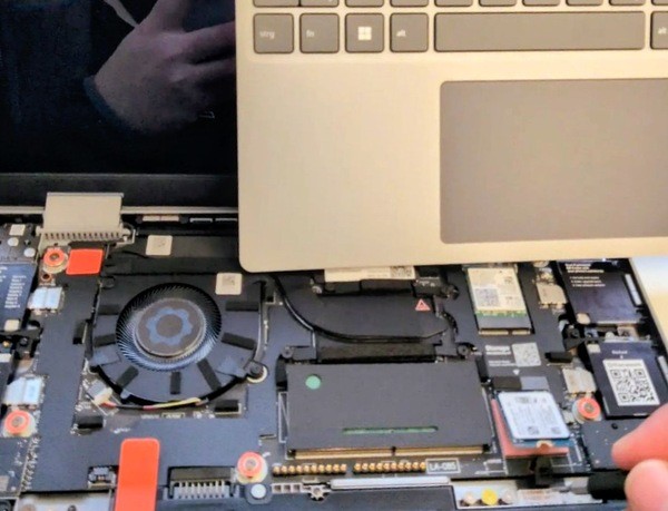 Geöffneter Framework 12, Oberseite mit Tastatur steht hochkant auf dem Mainboard, CPU-Lüfter ist zu sehen, während die kleine SSD ausgebaut wird.