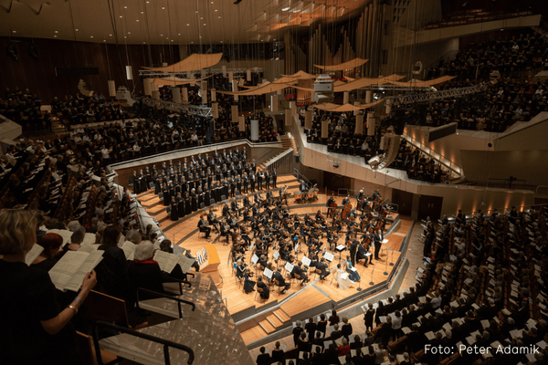 Berliner Philharmonie von Innen. Mit Menschen gefüllter Saal: Chor und Orchester auf der Bühne und singendes Publikum auf den Rängen. Foto von Peter Adamik