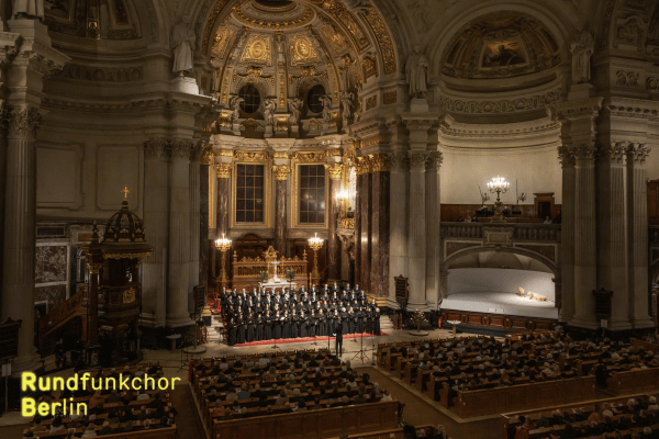 Der Rundfunkchor Berlin beim Weihnachtskonzert 2024 im Berliner Dom (c) Peter Adamik, Im Hintergrund sieht man die goldene Kuppel des Berliner Doms, im Vordergrund die Kirchenbänke und das Publikum. Die Atmosphäre ist feierlich (c) Peter Adamik
