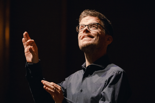 Chefdirigent Gijs Leenaars im Portrait während des Dirigierens, freudiger Gesichtsausdruck, schwarzer Hintergrund (c) Patricia Haas
