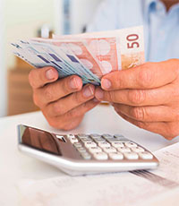 Zwei Hände halten aufgefächerte Euroscheine, darunter liegt ein Taschenrechner. Foto: LDprod/Shutterstock.com.