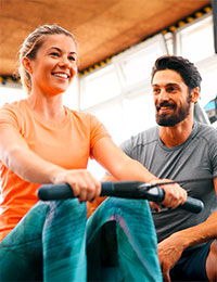 Ein Traineriunterstützt eine Frau bei einer Rückenübung.