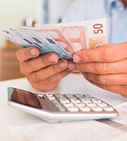 Zwei Hände halten Euro-Geldscheine, darunter liegt ein Taschenrechner. Foto: LDprod/Shutterstock.com.
