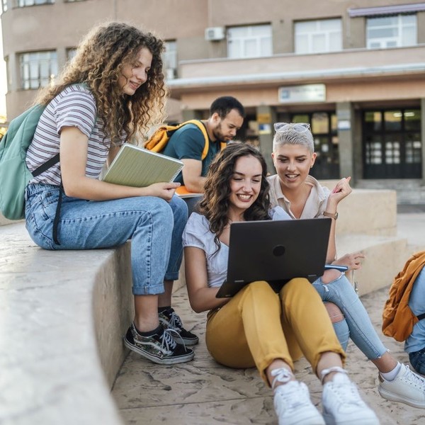 Eine Gruppe Studierender sitzt zusammen draußen und blickt in einen Laptop