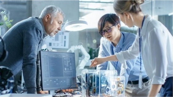 Three coworkers around a desk with a computer screen