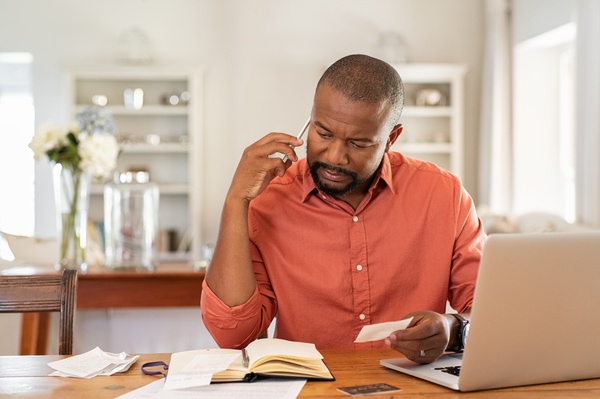A man sitting at a table with a laptop, a book and paperwork in front of him