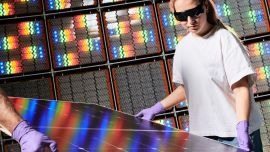 Two people with gloves carrying a solar panel, with more panels in the background