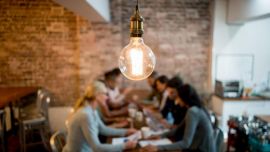A lightbulb hanging from the ceiling, in the background a group of people sitting at a table