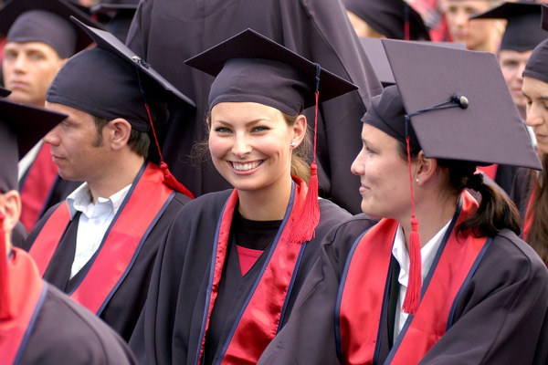 A group of graduates in caps and gowns stand together, smiling during a graduation ceremony.