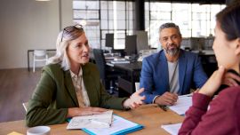 Two people in professional attire talking to a woman across a desk