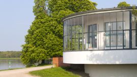 A round, glass-fronted building overlooking a lake