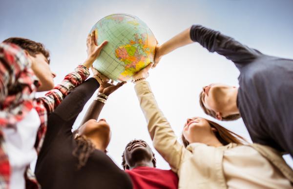Eine Gruppe junger Menschen hält gemeinsam einen bunten Globus empor. Jeder von ihnen berührt den Globus mit einer Hand, das Foto ist von unten aus der Mitte der Gruppe fotografiert.