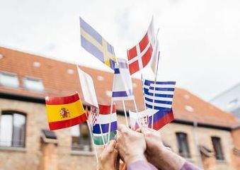 Zu sehen sind viele, kleine, europäische Landesflaggen, die von Händen in die Luft gehisst werden.