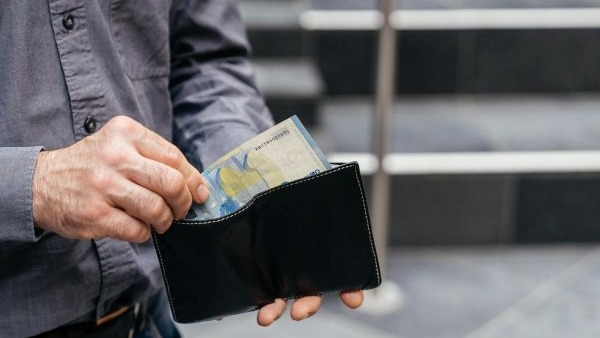 Nahaufnahme eines Portemonnaies, aus dem eine Person einen Geldschein entnimmt.