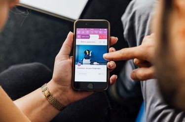 Zwei Personen sitzen nebeneinander, eine Person bedient ein Smartphone, während eine zweite Person mit auf den Bildschirm blickt. Der Fokus liegt auf dem Smartphone-Bildschirm.