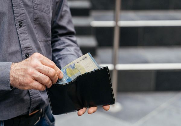 Nahaufnahme einer männlichen Hand, die einen Geldschein aus einem Portemonnaie zieht.