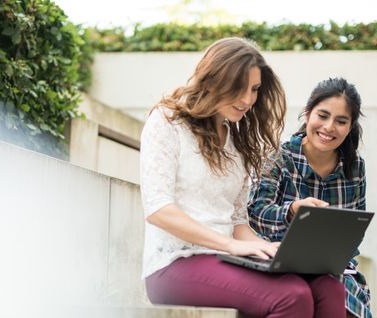Zwei Frauen schauen gemeinsam lächelnd auf den Bildschirm eines Laptops.