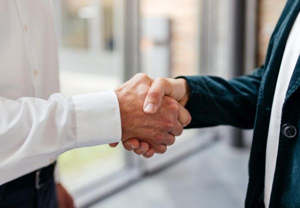 Nahaufnahme von zwei Händen, die sich zum Handschlag treffen und eine Partnerschaft, Zusammenarbeit oder Vereinbarung besiegeln.