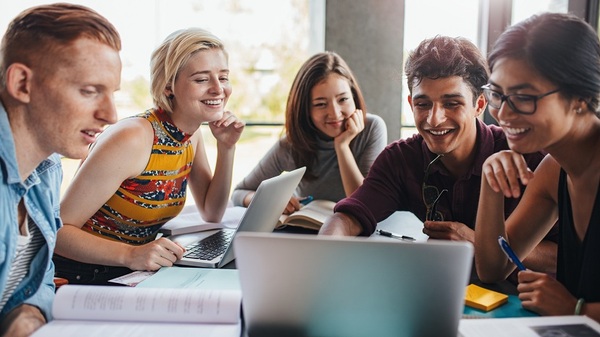 Fünf Studierende sitzen gemeinsam an einem Tisch und arbeiten an einem Laptop. Die Gruppe wirkt konzentriert und engagiert und steht für internationale Zusammenarbeit, gemeinsames Lernen und Austausch.