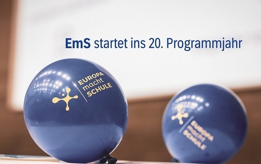 Zwei blaue Luftballons mit gelbem EmS-Logo vor unscharfem Hintergrund.