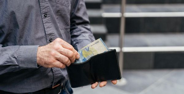Nahaufnahme eines Portemonnaies, aus dem eine Person einen Geldschein entnimmt.