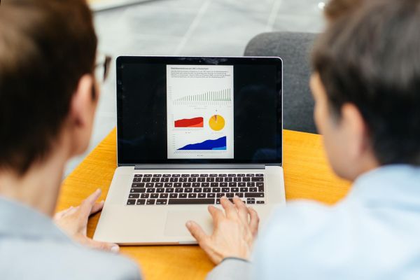 Zwei Menschen schauen auf einen Laptopbildschirm auf dem Statistiken und Diagramme zu sehen sind.