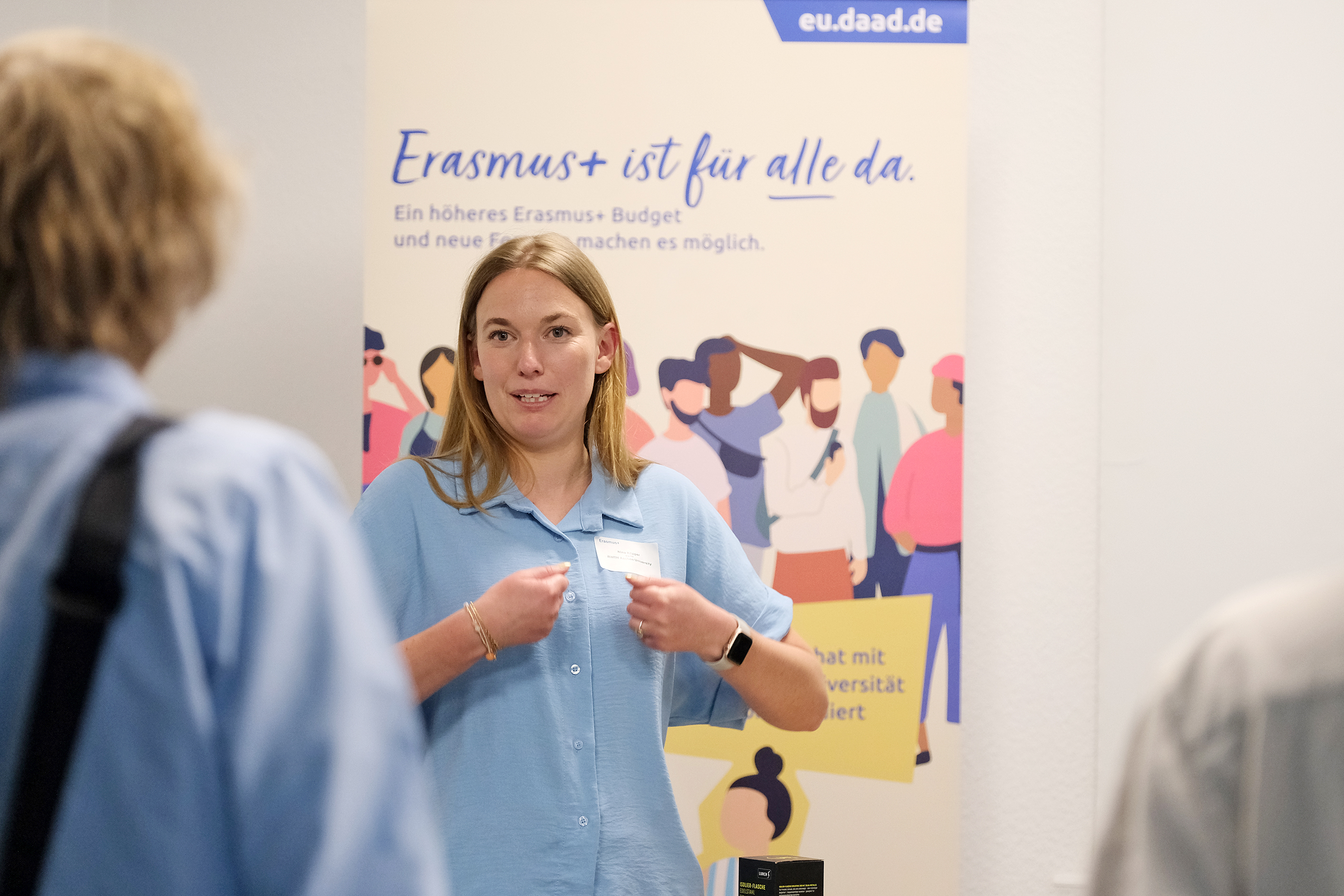 Eine Teilnehmende spricht und steht vor einem Erasmus+ Roll-Up.