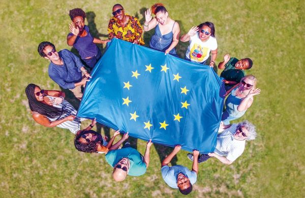 Eine Gruppe intenationaler Stundenten formt einen Kreis und hält eine Europa-Flagge gespannt in ihrer Mitte.