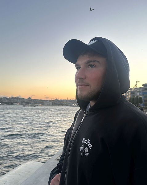 Der Studierende Marcel Nashwan steht in einer dunklen Kapuzenjacke am Ufer des Bosporus in Istanbul und blickt bei Sonnenuntergang über das Wasser; im Hintergrund sind die Silhouette der Stadt und ein vorbeifliegender Vogel zu sehen.