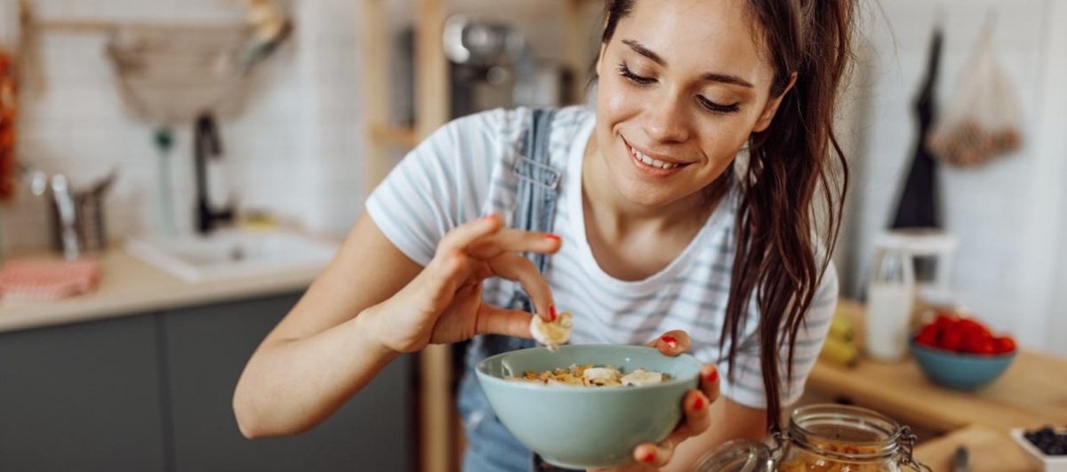 Junge Frau mit einer Schüssel Joghurt und Obst in der Hand.