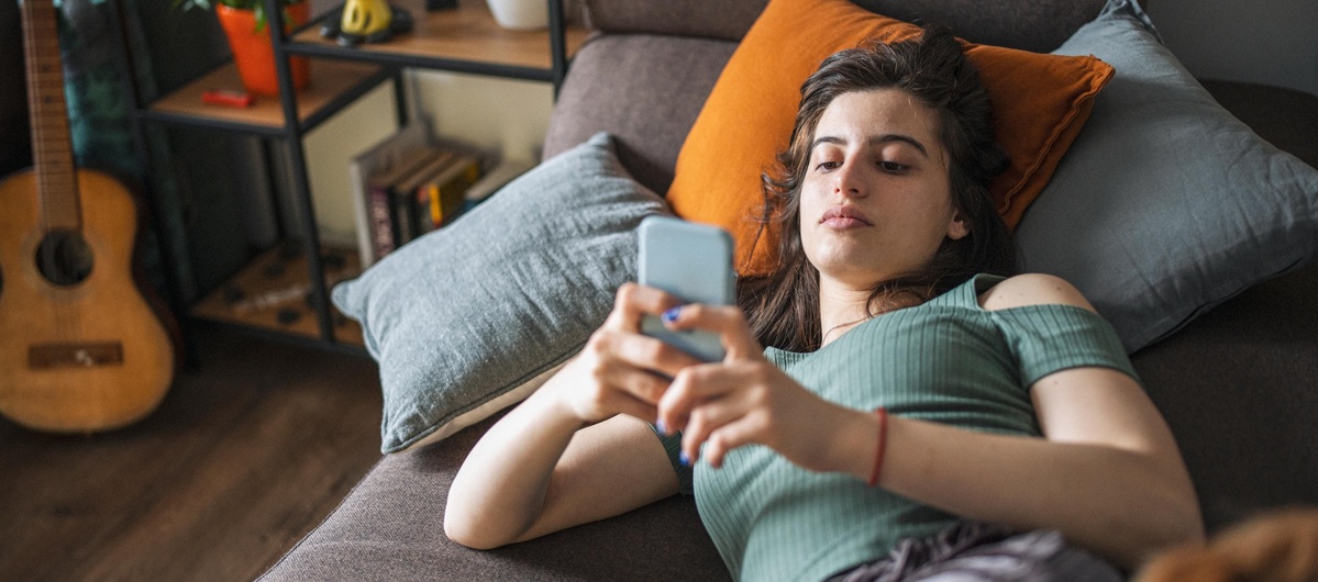 Junge Frau liegt auf dem Sofa und schaut aufs Handy