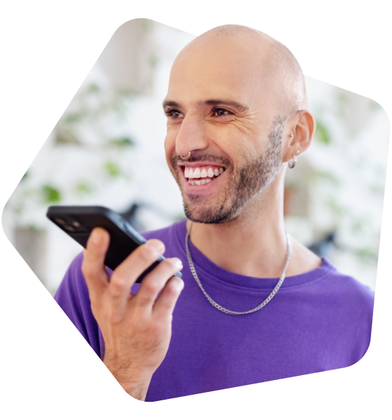 Junger Mann mit Glatze und Piercing lacht und hält ein Handy in der Hand.